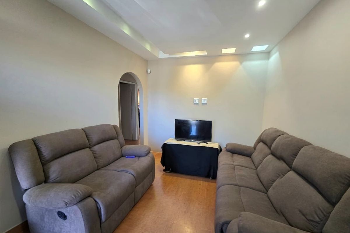 A living room featuring recessed ceiling lighting, cove lighting, and an arched doorway leading to an adjacent space.