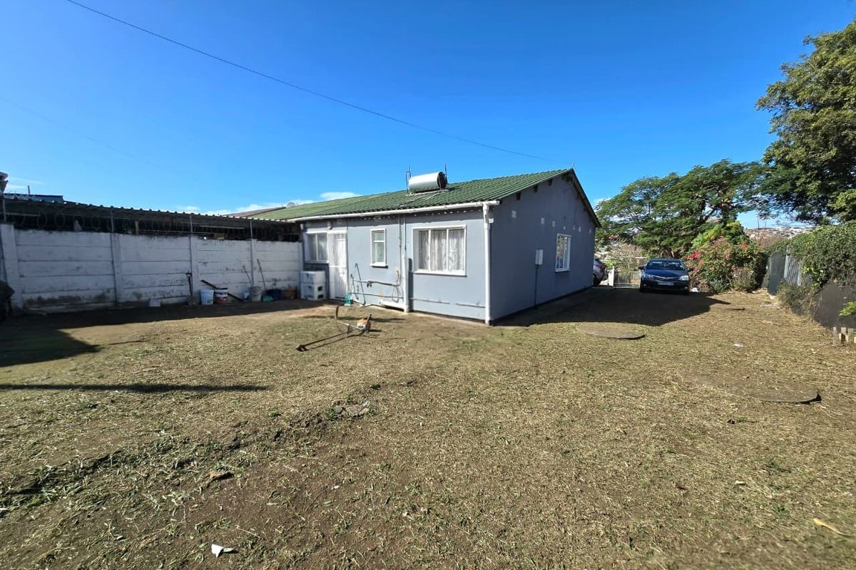 Rear view of the property featuring a large yard, solar water heater, and perimeter walling with security fencing.