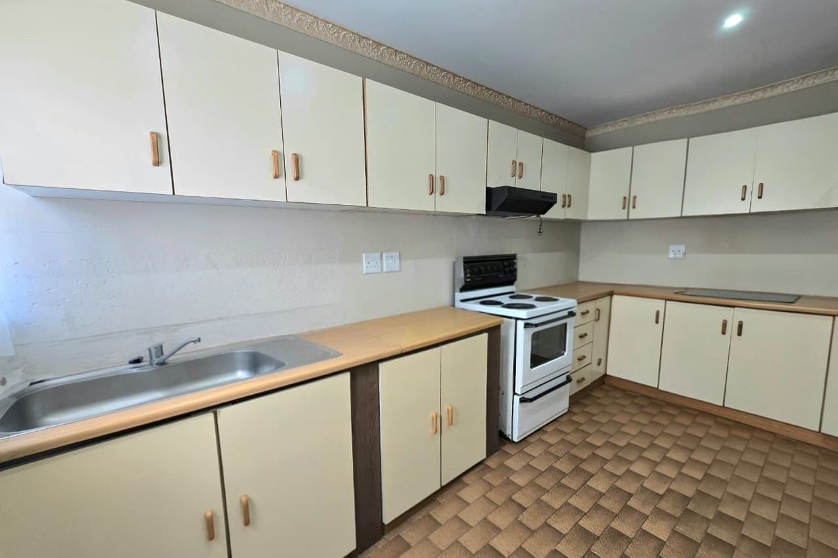 A functional kitchen featuring ample built-in cabinetry, laminate countertops, a stainless steel sink, and a freestanding stove with an extractor fan.