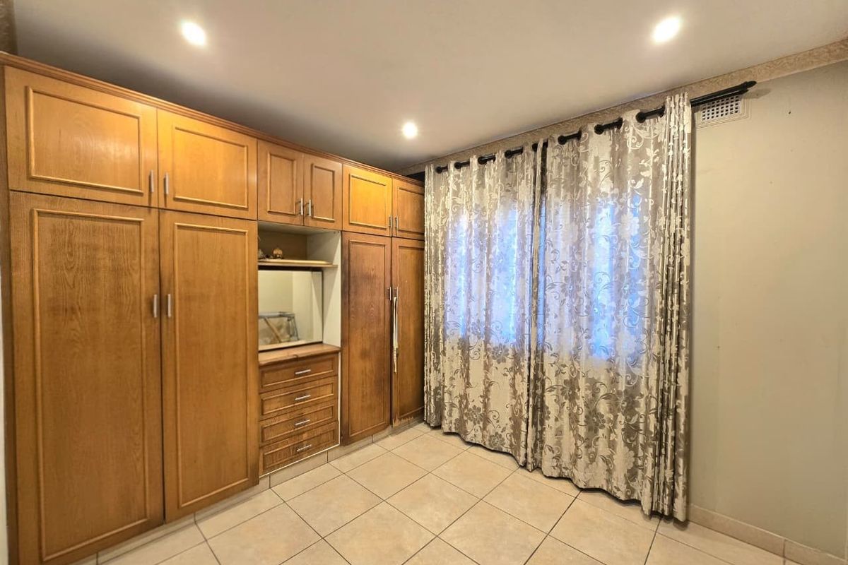 A bedroom featuring extensive built-in wooden cabinetry, tiled flooring, and recessed lighting, offering a functional and neutral space ready for personalization.