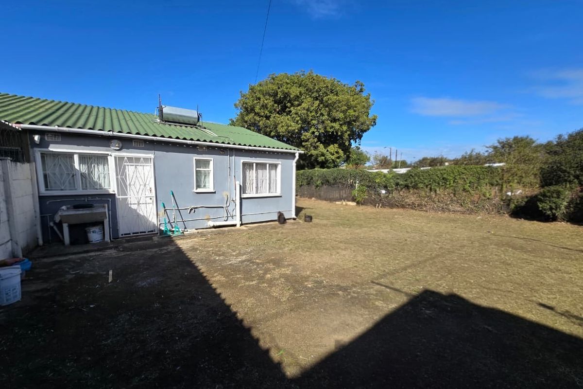 Rear view of the property featuring a corrugated roof, solar water heater, and a spacious backyard area with an external wash basin.