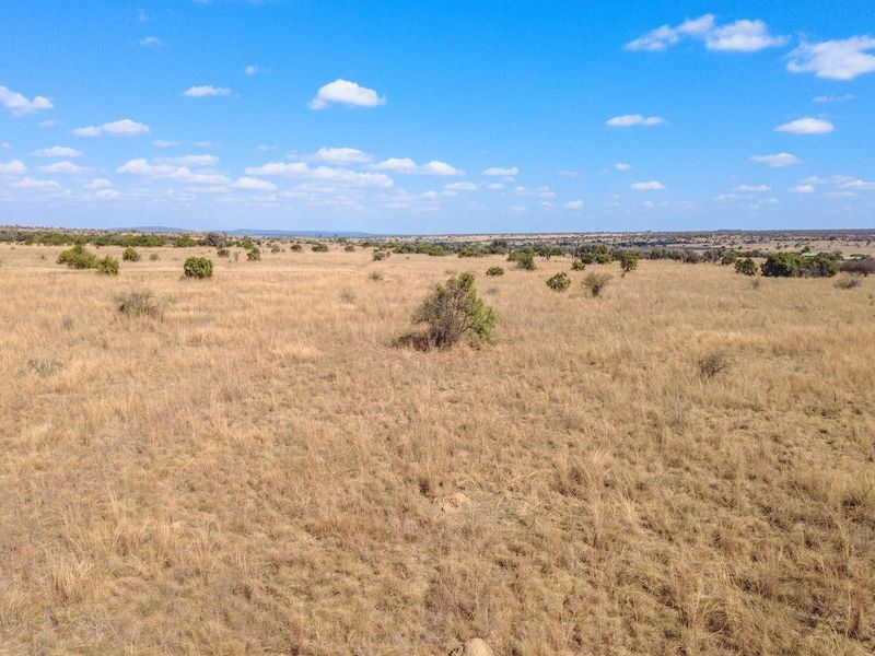 An aerial view of expansive, undeveloped residential land featuring natural grassland and scattered native vegetation under a clear blue sky.