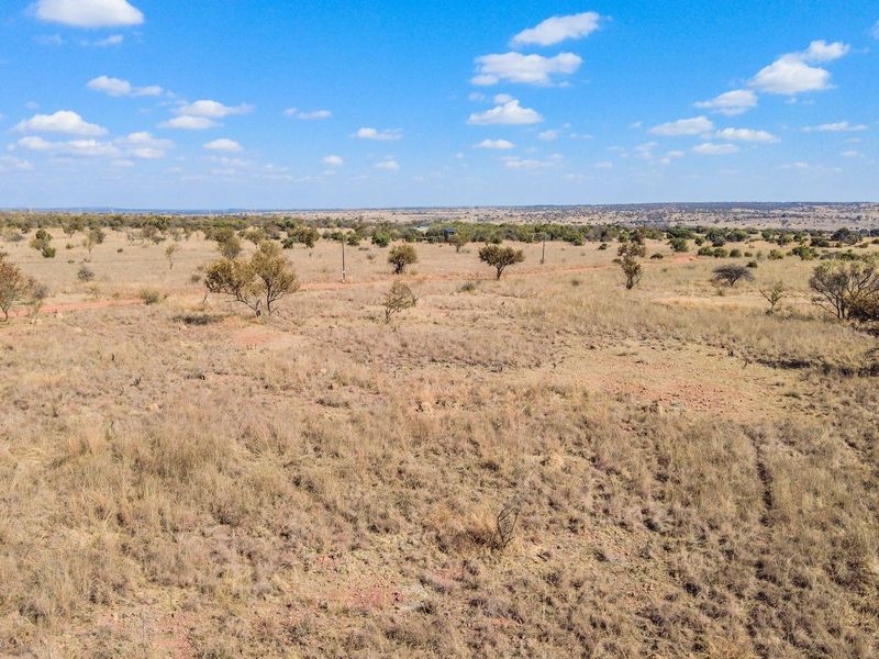 An aerial view of a large, undeveloped residential land parcel featuring native vegetation and open terrain under a clear blue sky.
