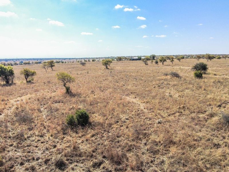 An aerial view of a large, undeveloped residential plot featuring natural dry grassland and scattered native trees.