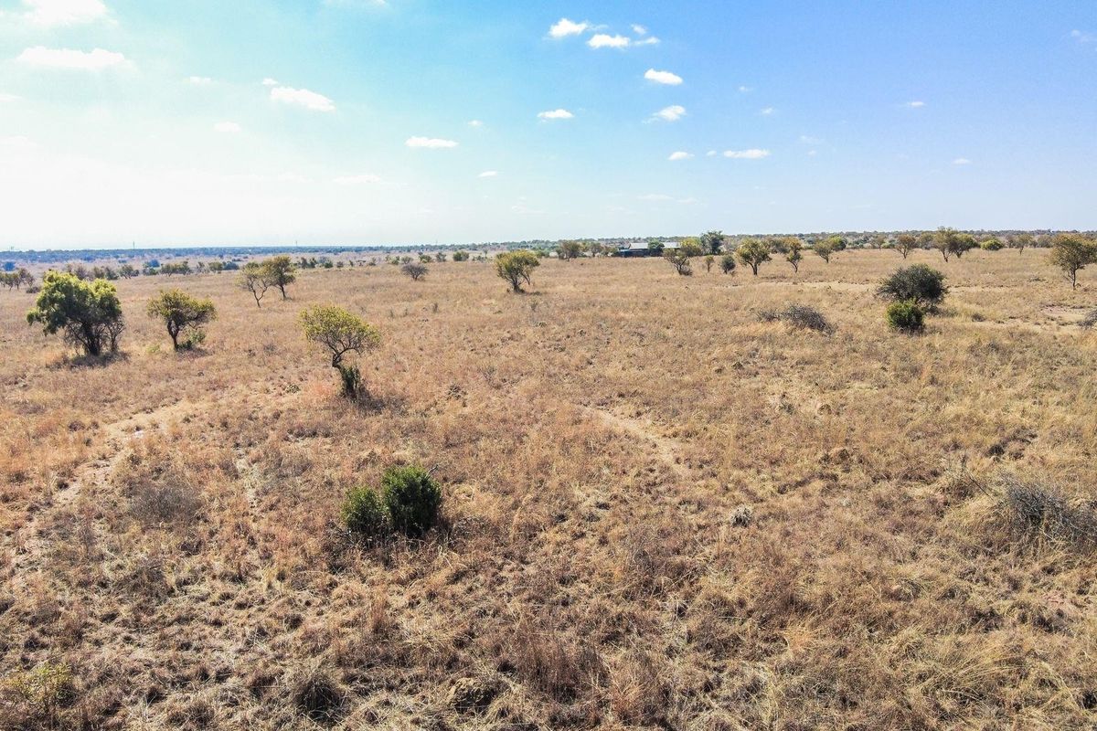 An aerial view of a large, undeveloped residential plot featuring natural dry grassland and scattered native trees.