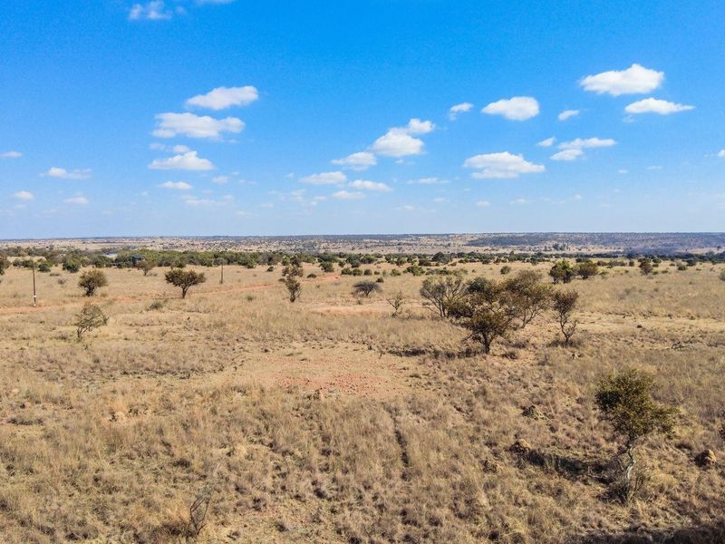 An aerial view of a vast, undeveloped residential plot featuring native vegetation and open landscape under a clear blue sky.