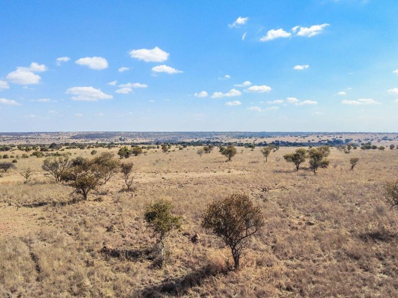 An aerial view of a vast, open residential land plot featuring natural vegetation and expansive landscape views.