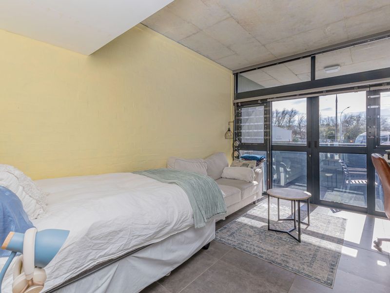 A bedroom featuring an exposed concrete ceiling, tiled flooring, and large glass sliding doors providing access to an outdoor area.