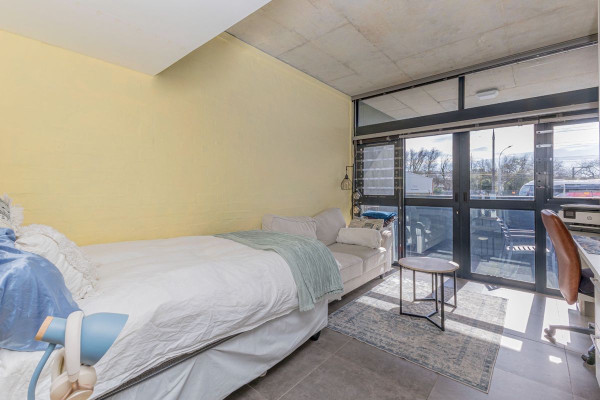 A bedroom featuring an exposed concrete ceiling, tiled flooring, and large glass sliding doors providing access to an outdoor area.