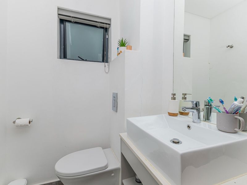 Compact bathroom featuring a modern wall-hung toilet, vanity basin with chrome mixer tap, and a large wall mirror.