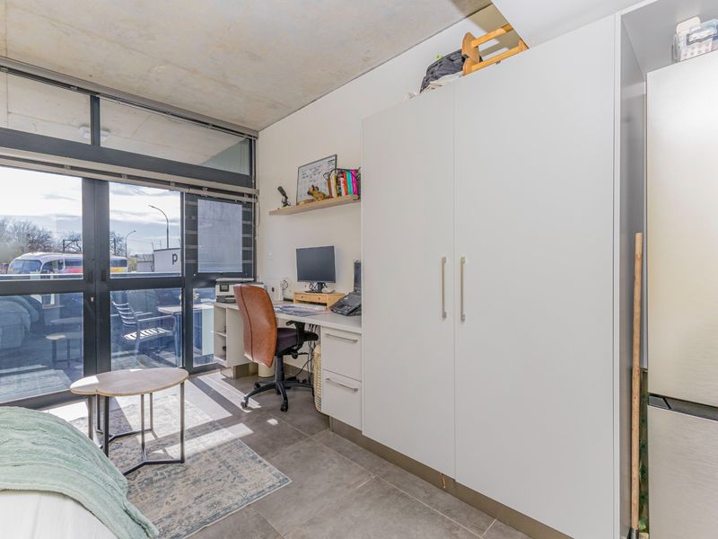 Modern bedroom featuring an exposed concrete ceiling, tiled flooring, built-in wardrobe, integrated desk space, and large sliding glass doors leading to a balcony.