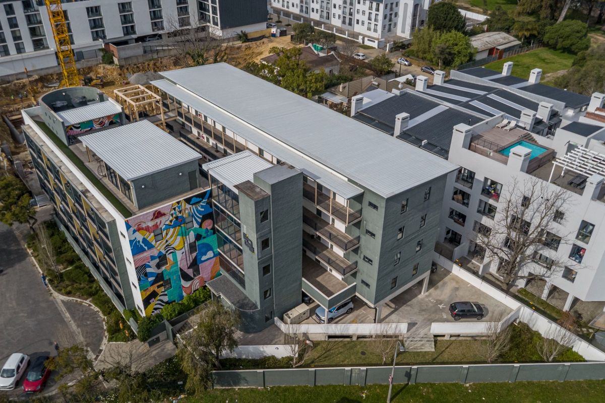 Aerial view of a modern multi-story apartment complex featuring a distinctive mural, private balconies, and an on-site parking area.