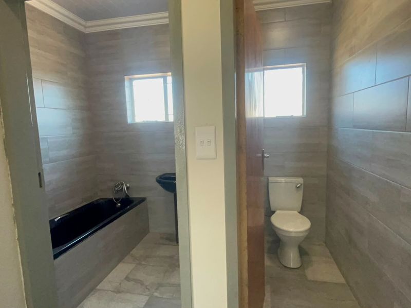 A modern bathroom featuring tiled walls and floors, a built-in bathtub, a pedestal basin, and a separate toilet area.