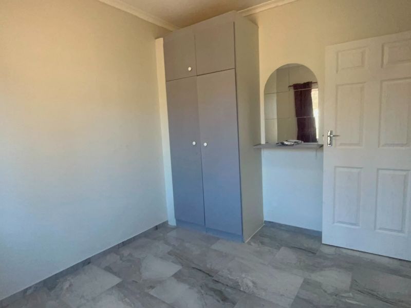 A clean, empty bedroom featuring tiled flooring, a built-in wardrobe, and a decorative arched mirror vanity area.