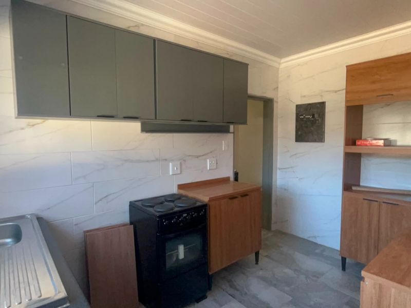 A functional kitchen space featuring marble-look wall tiles, built-in cabinetry, a stainless steel sink, and a freestanding stove.