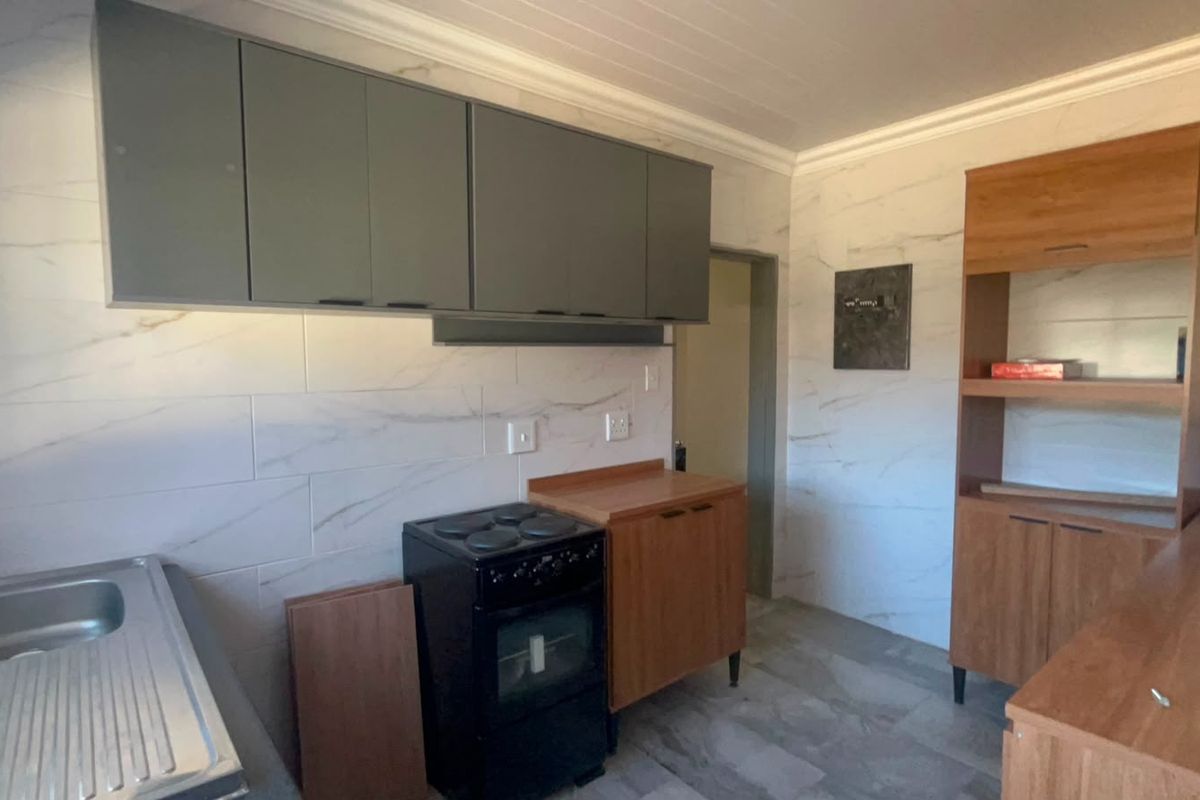 A functional kitchen space featuring marble-look wall tiles, built-in cabinetry, a stainless steel sink, and a freestanding stove.