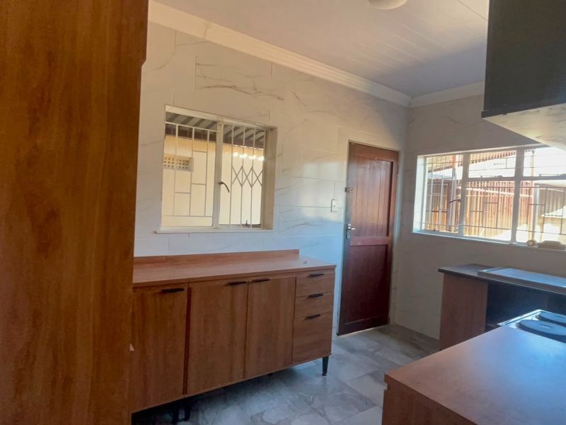 A functional kitchen featuring built-in wooden cabinetry, a hob with an extractor fan, tiled walls, and security bars on the windows.