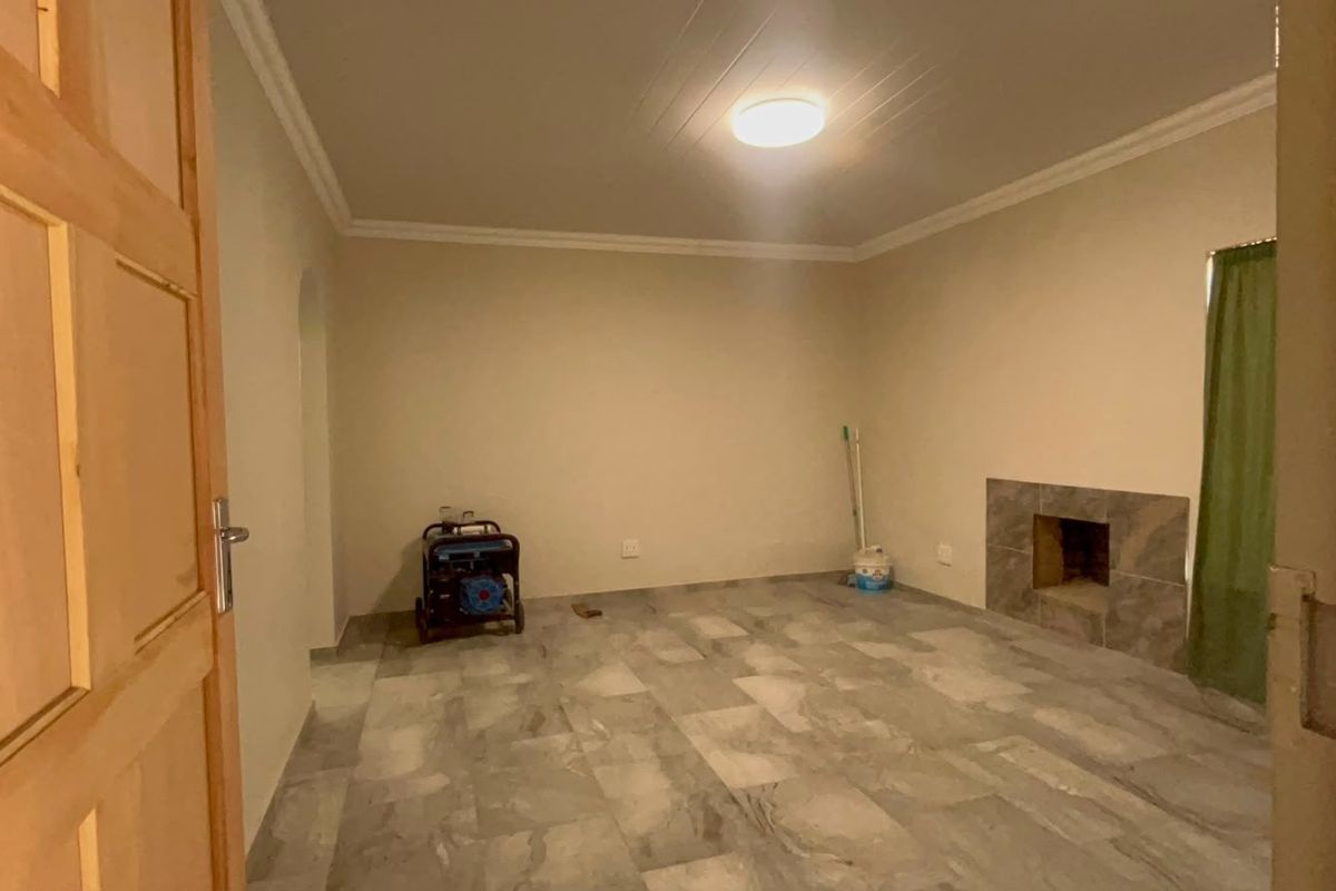 A spacious, empty living room featuring tiled flooring and a built-in fireplace, offering a neutral canvas for interior design.