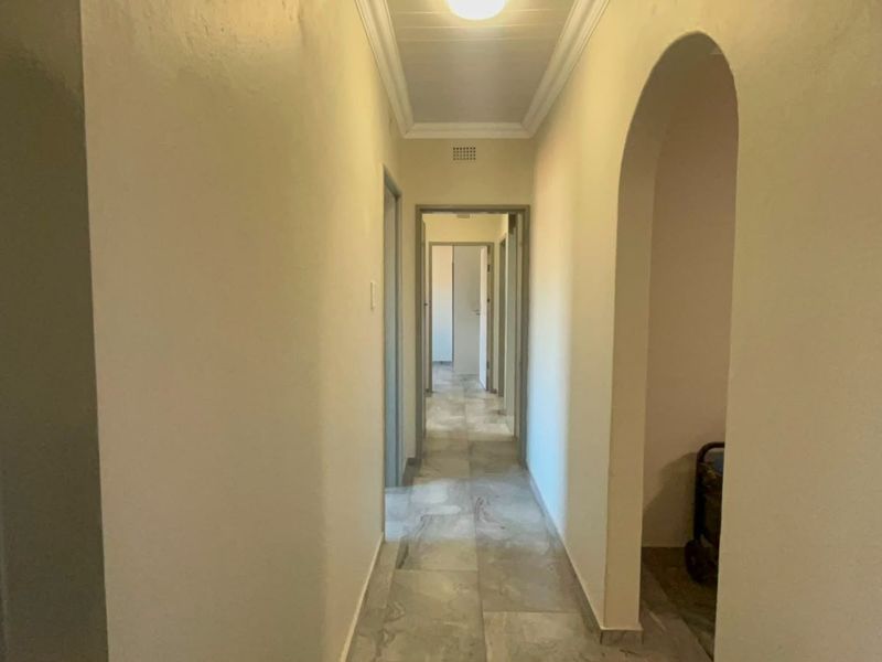 A bright, neutral-toned hallway featuring tiled flooring, an arched entryway, and classic ceiling cornicing, providing a clean transition between living spaces.