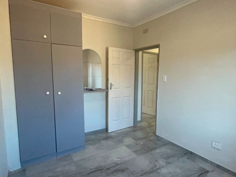 A clean, empty bedroom featuring neutral walls, tiled flooring, and built-in cupboards, offering a versatile space ready for personalization.