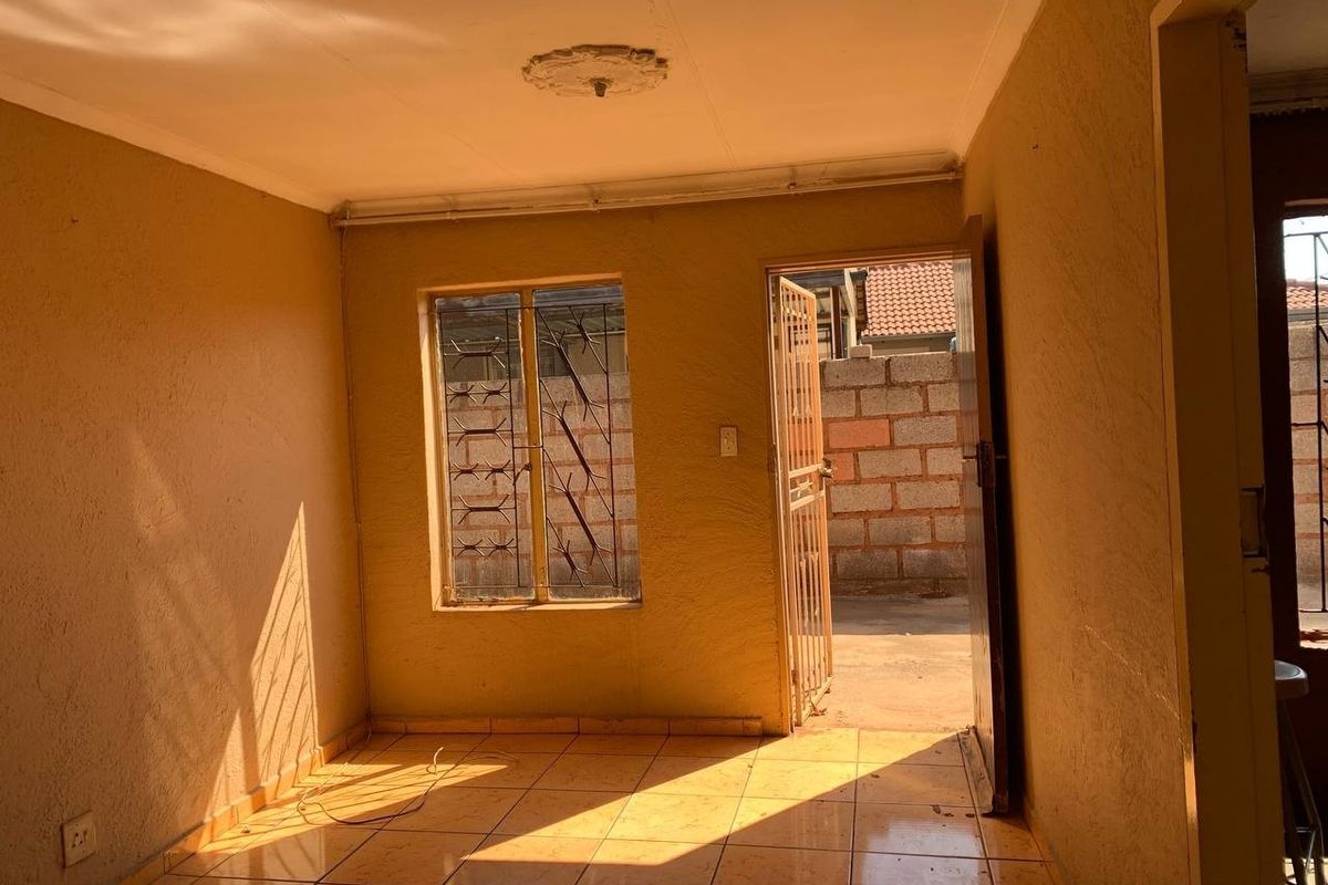 An empty living room featuring tiled flooring, security gates, and burglar bars, offering a blank canvas for renovation and interior design updates.