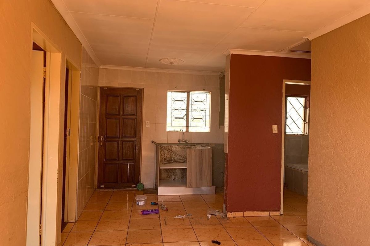 An empty kitchen area featuring tiled flooring, a basic sink unit, and tiled splashbacks, requiring significant renovation and cosmetic updates.