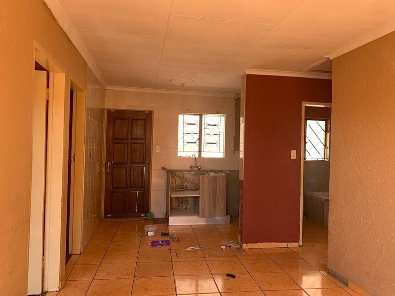 An empty kitchen area featuring tiled flooring, a basic sink unit, and tiled splashbacks, requiring significant renovation and cosmetic updates.