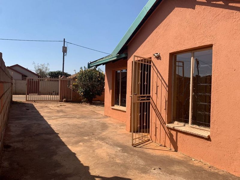 Rear exterior view of the property featuring a concrete driveway, security gate, and perimeter walling.