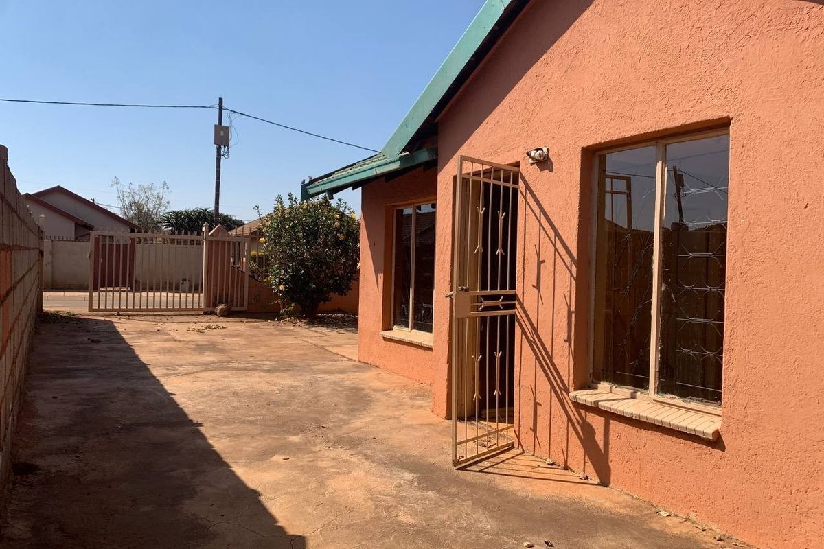 Rear exterior view of the property featuring a concrete driveway, security gate, and perimeter walling.