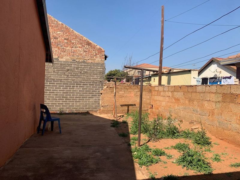 A rear exterior view of the property featuring a concrete patio area, a brick boundary wall, and a metal washing line.