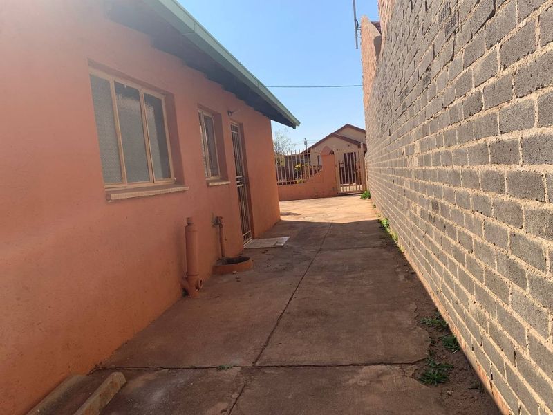 A narrow side passage featuring concrete paving, a brick boundary wall, and exterior access to the property with metal security fixtures.