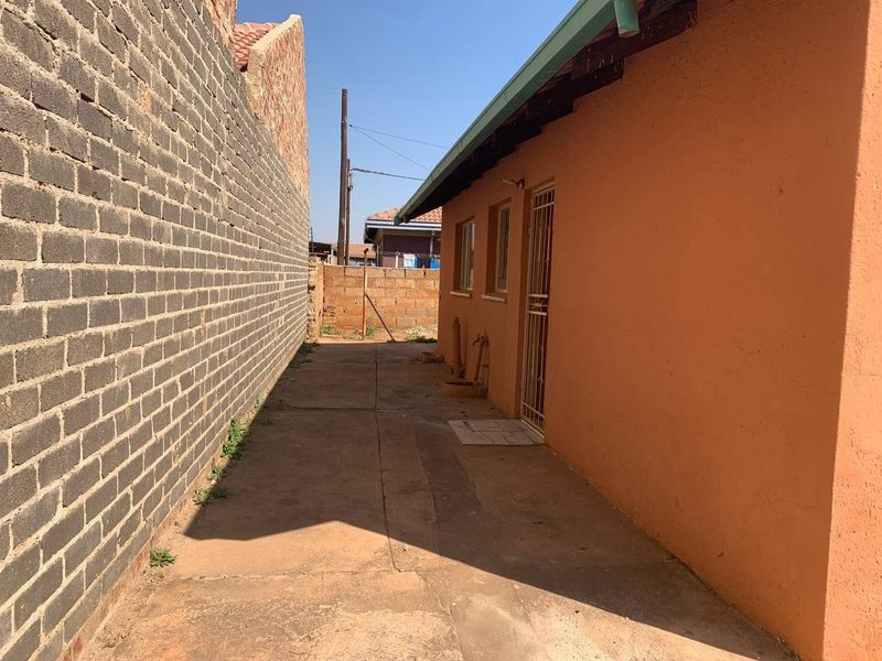 A narrow rear exterior walkway featuring concrete paving, a brick boundary wall, and an external water tap along the side of the house.