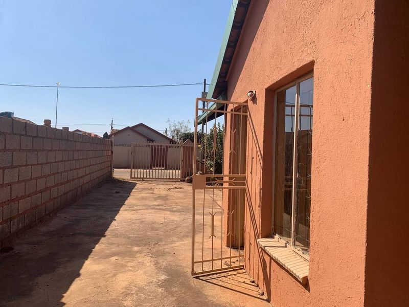 A view of the rear exterior area featuring a concrete paved yard, perimeter wall, and security gate access to the property.