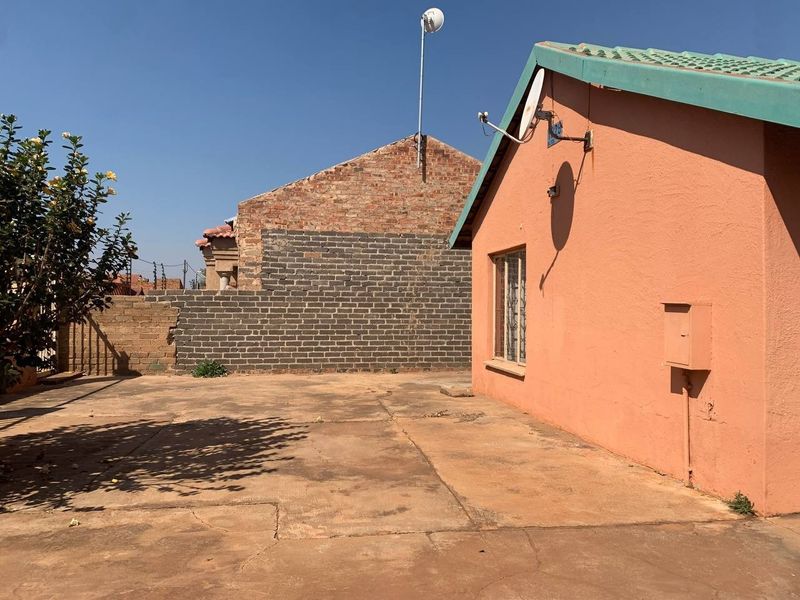 Rear exterior view of the property featuring a concrete paved yard, brick boundary wall, and exterior wall finishes.