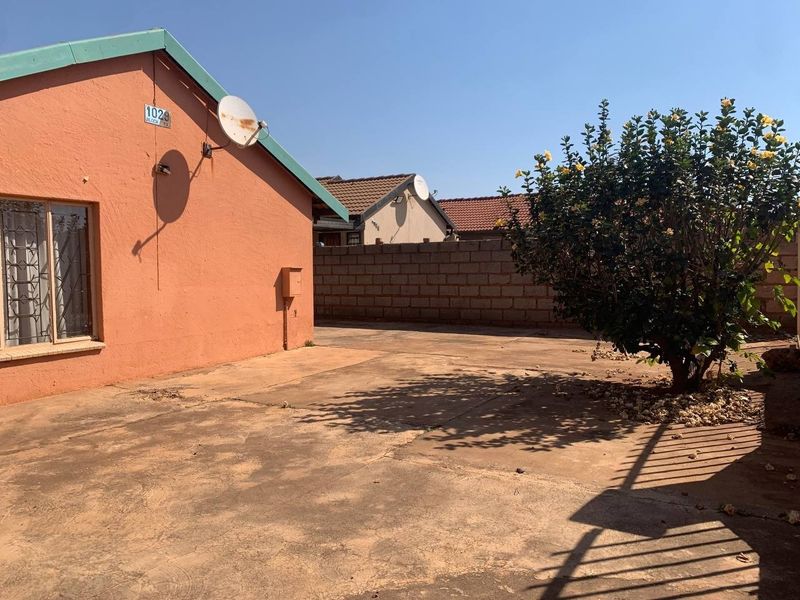 Rear exterior view of the property featuring a concrete paved yard, perimeter masonry wall, and security bars on the windows.