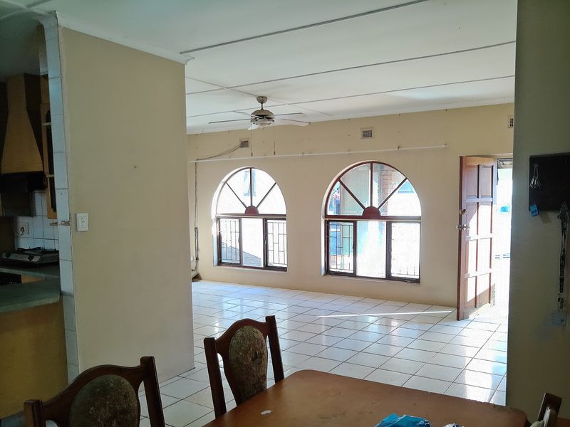 Open plan living and kitchen area featuring ceramic tile flooring, distinctive arched windows, and a ceiling fan, offering a blank canvas for renovation.