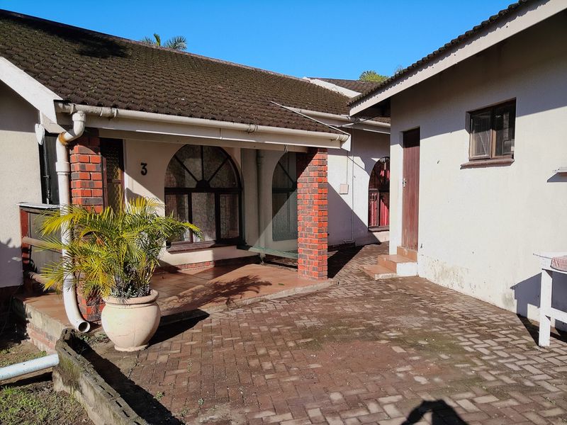 A rear courtyard area featuring brick paving, arched windows, and covered patio space with brick pillar supports.