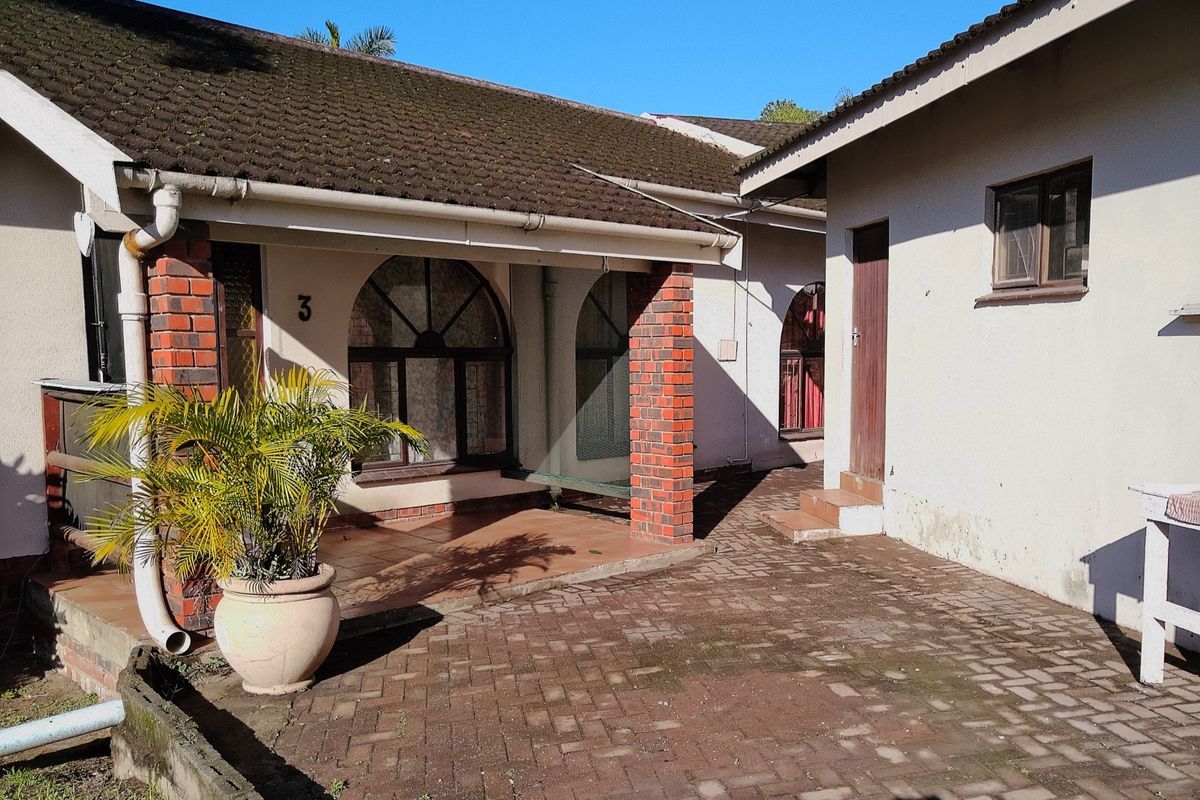 A rear courtyard area featuring brick paving, arched windows, and covered patio space with brick pillar supports.