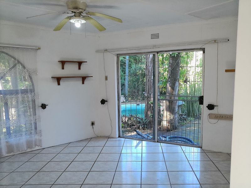 An empty living room featuring ceramic floor tiles, a ceiling fan, and sliding glass doors providing direct access to the outdoor pool area.