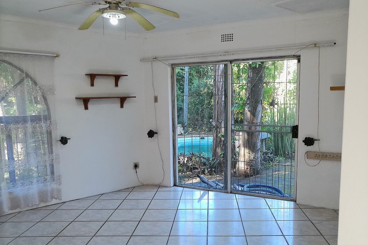 An empty living room featuring ceramic floor tiles, a ceiling fan, and sliding glass doors providing direct access to the outdoor pool area.
