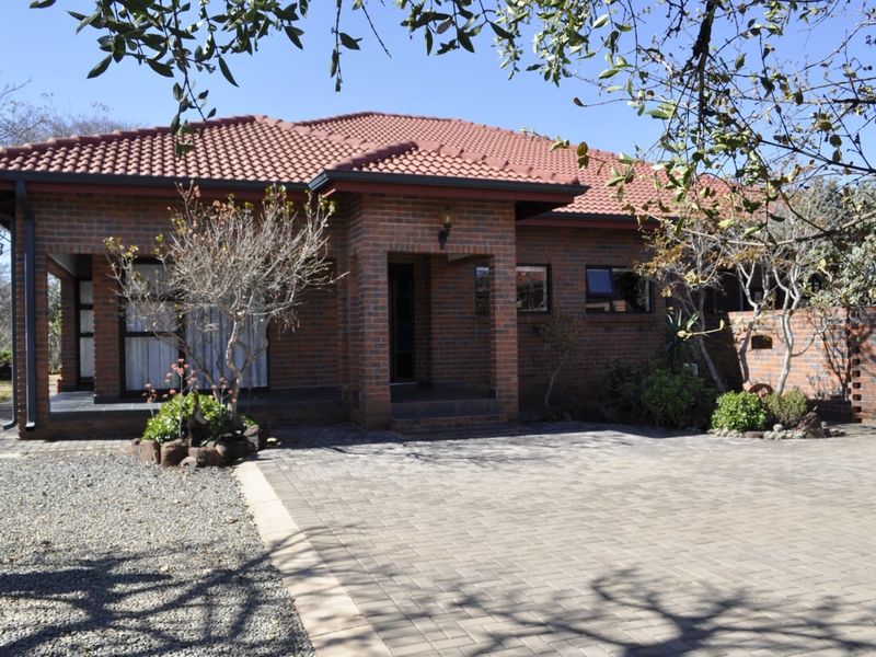 A well-maintained single-story face brick house featuring a tiled roof, paved driveway, and a covered entrance porch.