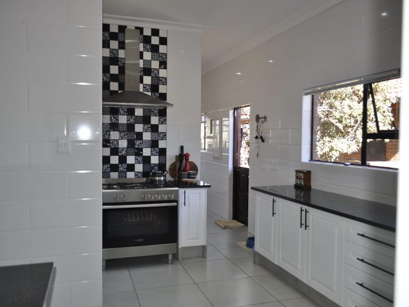 A functional kitchen featuring white cabinetry, dark granite countertops, a gas stove with a stainless steel extractor fan, and a distinctive checkered tile splashback.