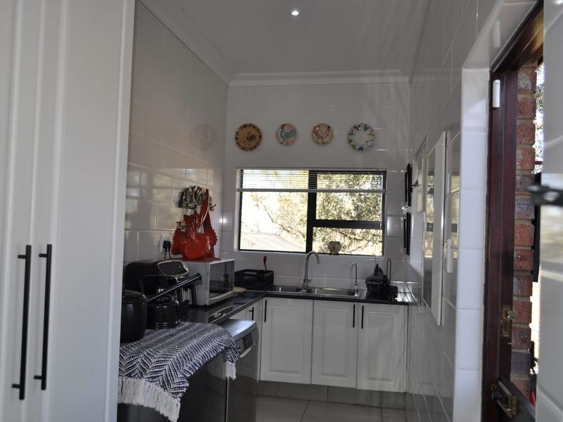 A functional scullery featuring white cabinetry, tiled walls, and a stainless steel sink, providing additional prep and wash-up space.