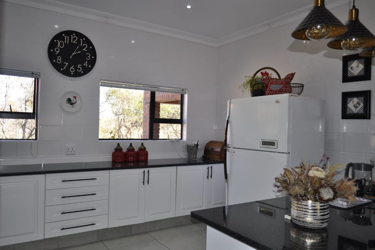 A well-maintained kitchen featuring white cabinetry, dark granite countertops, tiled splashbacks, and modern aluminium window frames with natural light.