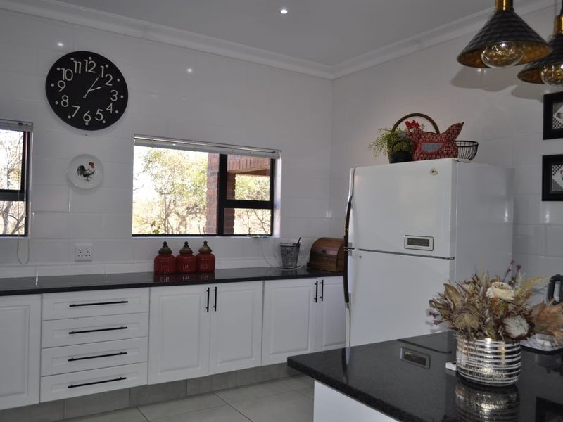 A well-maintained kitchen featuring white cabinetry, dark granite countertops, tiled splashbacks, and modern aluminium window frames with natural light.