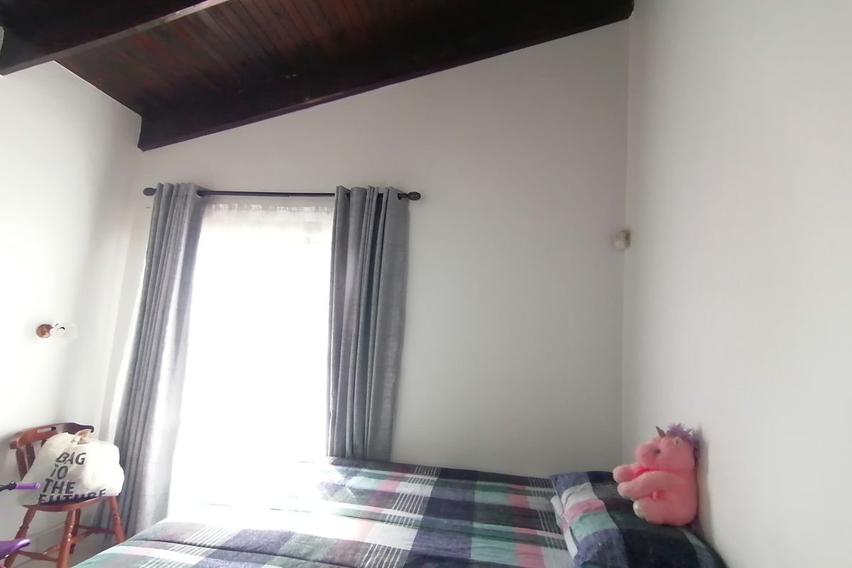 A bedroom featuring a high, sloped ceiling with exposed timber beams and natural light from a window.