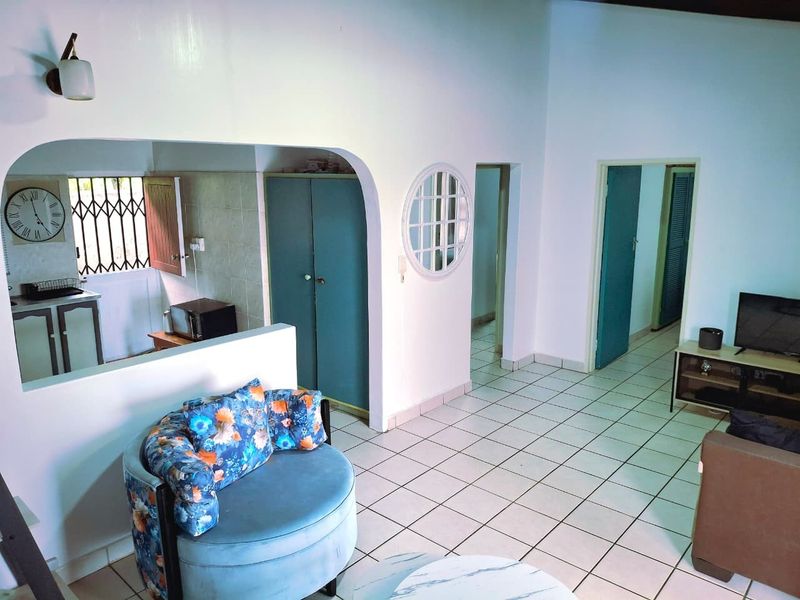 Open plan living area featuring tiled flooring, an arched pass-through to the kitchen, and access to internal rooms.