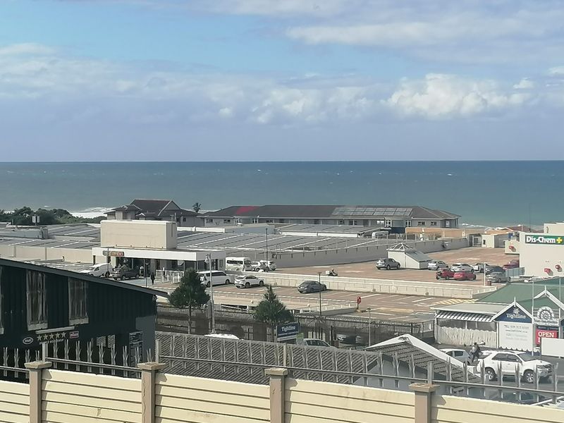An elevated view overlooking a commercial area and parking lot with the ocean visible in the background.
