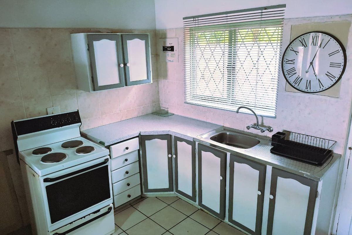 A functional kitchen featuring a freestanding stove, stainless steel sink, tiled splashback, and built-in cabinetry with security bars on the window.