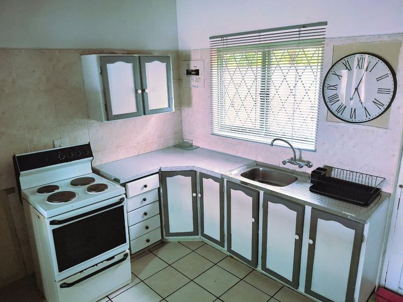 A functional kitchen featuring a freestanding stove, stainless steel sink, tiled splashback, and built-in cabinetry with security bars on the window.